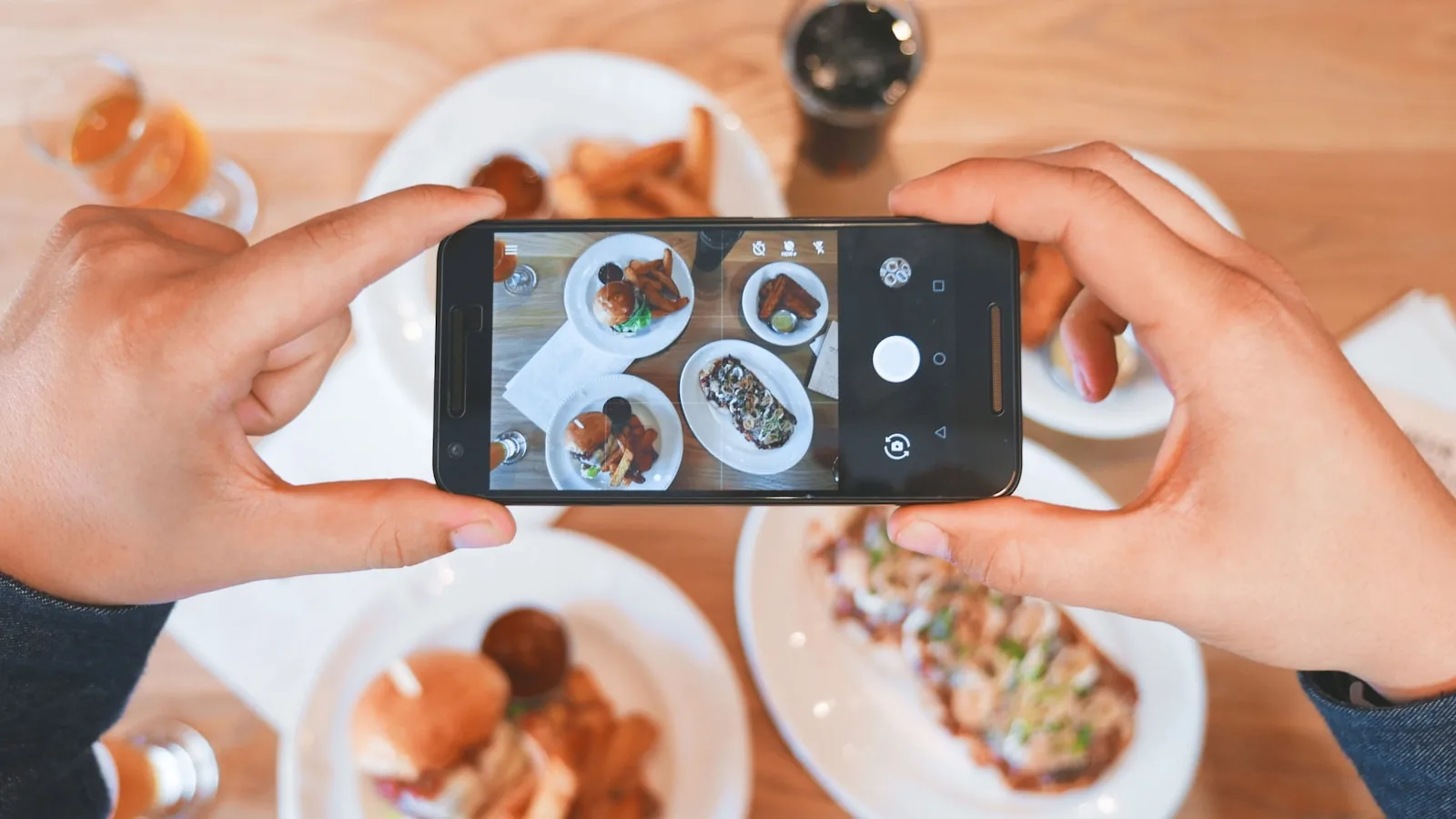 Telefonla yemek fotoğrafı çeken bir kişi